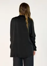 Camisa de satén color negro con cuello mao y volados en las mangas. Presenta cierre frontal con botones y diseño de corte holgado con largo asimétrico.
