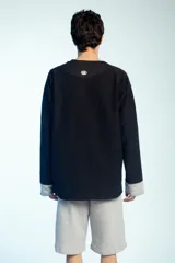 Buzo de felpa negro de corte oversize, con cuello redondo y mangas largas con puños grises doblados hacia afuera. Presenta costuras externas decorativas en tono gris claro a lo largo de las mangas y los hombros.