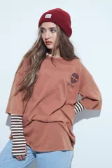 Remera de corte oversize color marrón con efecto gastado, manga corta y estampa gráfica retro en el frente.