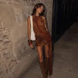 Vestido corto de cuello halter con estampado abstracto en tonos marrones y naranjas. Presenta un diseño ajustado con un detalle de nudo lateral y una caída de tela asimétrica con bordes ondulados.