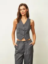 Chaleco de sastrería gris oscuro con diseño de rayas verticales finas, escote en V y cierre frontal con tres botones. Presenta un corte entallado y bolsillos decorativos en la parte inferior.
