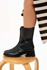 Bota de caña media color negro con textura de reptil, confeccionada en cuero. Presenta horma cuadrada, cierre lateral interno, taco cuadrado y una pequeña plataforma.