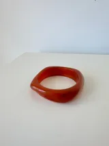 Pulsera rígida de acrílico en color naranja rojizo, con diseño asimétrico y acabado brillante.