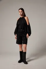 Bermuda de jean negro, de calce bajo y corte ancho a la rodilla, con tachas metálicas plateadas distribuidas por toda la prenda.