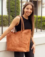 Bolso tipo shopper de cuero, color marrón tostado, con detalle de costura artesanal en el borde superior y correas largas para llevar al hombro.