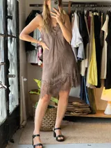 Vestido corto lencero de color marrón con detalles de encaje en el escote y en el ruedo asimétrico, tirantes finos y diseño fluido.