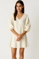 Vestido corto de lino color crema, con escote en V, mangas tres cuartos abullonadas con puños elásticos y costura central vertical.