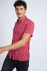 Camisa de manga corta con diseño a rayas verticales en color azul marino y blanco. Presenta cuello clásico, cartera abotonada frontal y logo bordado en el pecho. Posee un corte slim fit.