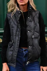 Chaleco puffer beige, sin mangas, con cuello alto, cierre frontal de cremallera y bolsillos laterales.