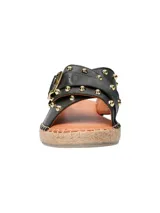 Sandalia tipo ojota con base de yute, tiras cruzadas de cuero negro con tachas doradas y hebilla metálica decorativa.