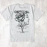 Remera gris claro jaspeado de algodón, corte oversize, con estampa en la espalda de una rosa combinada con el rostro de una mujer y texto con nombres de ciudades.