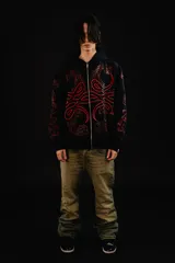 Hoodie con cierre frontal completo, confeccionado en algodón de tejido grueso. Presenta un diseño estampado en serigrafía con motivos de hojas de acanto en color rojo sobre fondo negro. Cuenta con bolsillos laterales y cierre metálico YKK.