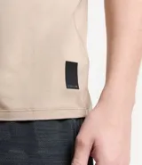 Remera deportiva de hombre con tecnología dry fit, cuello redondo y manga corta. Presenta un diseño liso en color beige con una pequeña etiqueta decorativa en el dobladillo.