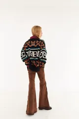 Sweater de punto oversize con diseño de intarsia geométrica y letras en tonos marrón, amarillo y rosado. Presenta cuello redondo, mangas largas y puños acanalados.