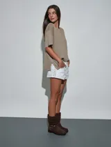 Short de jean blanco con tachas doradas decorativas en los bolsillos delanteros y en los laterales, talle medio y cierre frontal con botón y cremallera.