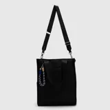Bolso tipo tote color negro, con diseño rectangular, asas de mano y correa larga ajustable e intercambiable con inscripciones de la marca. Incluye un bolsillo frontal abierto y un llavero decorativo de cuerda trenzada azul y beige.