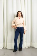 Polera de punto color manteca, con cuello alto, diseño de trenzas y flores en el frente, y mangas globo amplias.