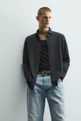 Camisa de corte relajado confeccionada en tejido de algodón con textura. Presenta cuello italiano, manga larga con puños abotonados y cierre frontal mediante botonadura.