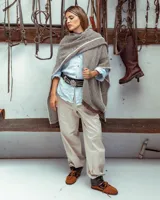 Ruana de silueta amplia y caída relajada, tejida en lana merino marrón y blanca con diseño de rayas y bordes desflecados.