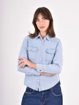 Camisa de jean en tono celeste claro, con cuello clásico, cierre frontal con botones metálicos y dos bolsillos frontales con solapa.