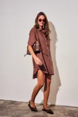 Vestido camisero corto de color marrón, con mangas cortas, cuello camisero, cierre frontal de botones y un bolsillo ojal en el pecho.