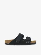 Sandalias Birkenstock modelo Uji de color negro, con dos tiras anchas ajustables mediante cierres de contacto y detalles de remaches metálicos. Confeccionadas con una combinación de gamuza y cuero nobuk, presentan la clásica plantilla anatómica de corcho y suela de goma negra.