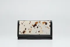 Billetera rectangular de cuero negro con solapa frontal en cuero con pelo estampado tipo animal print de manchas.