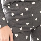 Pijama de dos piezas compuesto por una remera de manga larga con cuello redondo y un pantalón largo de corte recto, ambos confeccionados en tejido de punto gris con estampado de corazones blancos.