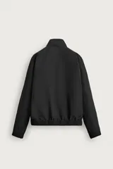 Cazadora bomber de corte relajado confeccionada en tejido técnico color negro. Presenta cuello subido, manga larga amplia, bolsillos de vivo en cadera, acabados elásticos y cierre frontal con cremallera de doble dirección.