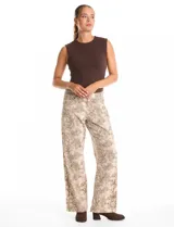 Jean de corte wide leg con estampado animal print de serpiente en tonos beige y gris. Presenta diseño clásico de cinco bolsillos, presillas para cinturón y cierre frontal con botón metálico.