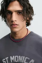 Camiseta de manga larga, corte ajustado (muscle fit), color gris oscuro con efecto lavado. Presenta un estampado frontal desgastado con el texto curvo "ST MONICA" en color plateado o gris claro.