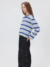 Remera de manga larga con diseño a rayas horizontales en tonos azul, blanco y negro. Presenta un cuello redondo al tono y un logo bordado en el pecho. El diseño destaca por tener un patrón de rayas diferente en las mangas y un calce holgado.