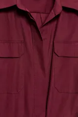 Vestido midi de estilo camisero color bordó, con cuello solapa, escote en pico y cierre frontal con botones ocultos. Presenta manga larga, bolsillos laterales ocultos, solapas decorativas en el pecho y cinturón de lazada en el mismo tejido.