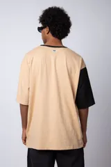 Remera de corte oversize en color beige, con cuello redondo en contraste negro y una manga en color negro. Presenta un pequeño estampado circular en el pecho con la frase 'Don't worry, be happy'.