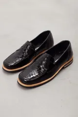 Mocasín de cuero vacuno en color marrón, con diseño bitono que combina texturas lisas y con grabado tipo cocodrilo en el empeine. Cuenta con detalle de estribo clásico y suela plana con vira en contraste.