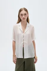 Blusa blanca de lyocell con cuello solapa, mangas cortas y cierre frontal mediante cordones para anudar.