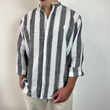 Camisa de manga larga con cuello mao, confeccionada en tejido de lino a rayas verticales en tonos blanco y celeste. Presenta cierre frontal con botones y corte clásico.