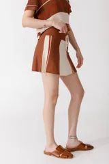 Falda corta de tejido de punto, color rojo coral, con un panel frontal en color rosado claro. Presenta un cordón de ajuste en la cintura y detalles de franjas verticales en verde azulado y rosado claro en el panel frontal.