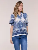 Blusa de crepe color blanco con estampado paisley en tonos azules y negros. Presenta cuello mao con escote en V, cierre frontal con botones y mangas cortas abullonadas con puños elastizados en punto smock.