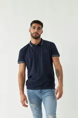 Remera polo negra de manga corta con ajuste regular. Presenta cuello y puños con ribete a rayas en gris y bordó. El logo de la marca está estampado en el pecho.