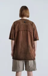 Remera de cuello redondo con calce oversize, confeccionada en algodón con proceso de teñido batik artesanal en tono óxido. Presenta costuras visibles y diseño de paneles en la parte superior.