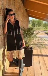 Vestido corto negro sin mangas, con escote en V y detalle de flecos en el ruedo. Presenta bordados en color blanco en el escote, los bolsillos y el centro del vestido.