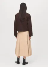 Chaqueta corta de algodón en color marrón oscuro, con cuello de efecto piel en tono contrastante. Presenta cierre frontal con cremallera y botones a presión, además de dos bolsillos frontales con solapa y cierre de botón.