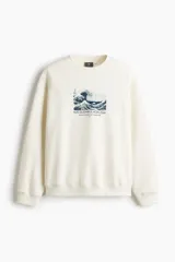 Buzo blanco off-white de corte holgado y hombros caídos, con cuello redondo, puños y bajo acanalados. Presenta un estampado frontal en el pecho inspirado en la obra de Katsushika Hokusai, 'La gran ola de Kanagawa'.