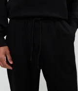 Pantalón de pijama tipo jogger, color negro, con cintura elástica ajustable mediante cordón, bolsillos laterales y puños en los tobillos.