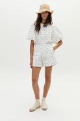 Short de tiro alto confeccionado en lino blanco con estampado de lunares azules. Presenta pinzas frontales y cierre con botones.