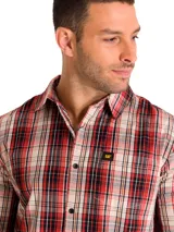 Camisa de manga larga con estampado a cuadros en tonos rojos, negros y beige. Presenta cuello clásico, cierre frontal con botones y un bolsillo en el pecho con etiqueta de la marca Caterpillar.
