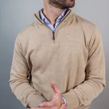 Buzo de punto color beige con cuello alto y medio cierre frontal.