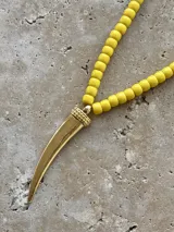 Collar de cuentas redondas color amarillo con dije colgante dorado en forma de cuerno.