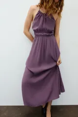 Vestido midi de color morado con cuello halter, tirantes finos ajustables y espalda descubierta. Cuenta con detalles fruncidos en el delantero y la cintura.